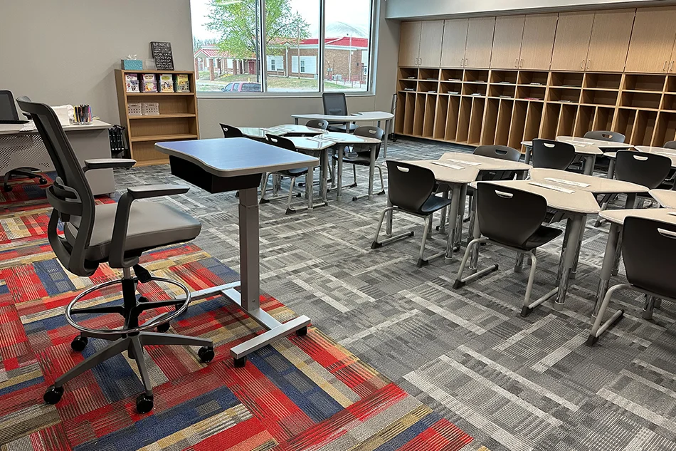 A teacher's chair and desk at the front of a classroom