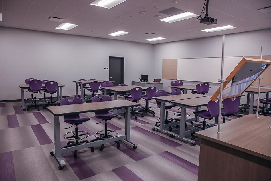 A classroom with adjustable tables and purple rolling chairs