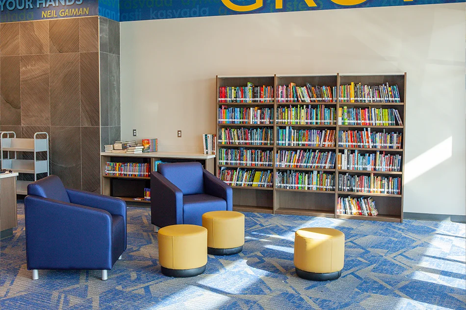 Two blue chairs with small yellow ottomans in front of a bookshelf in a library