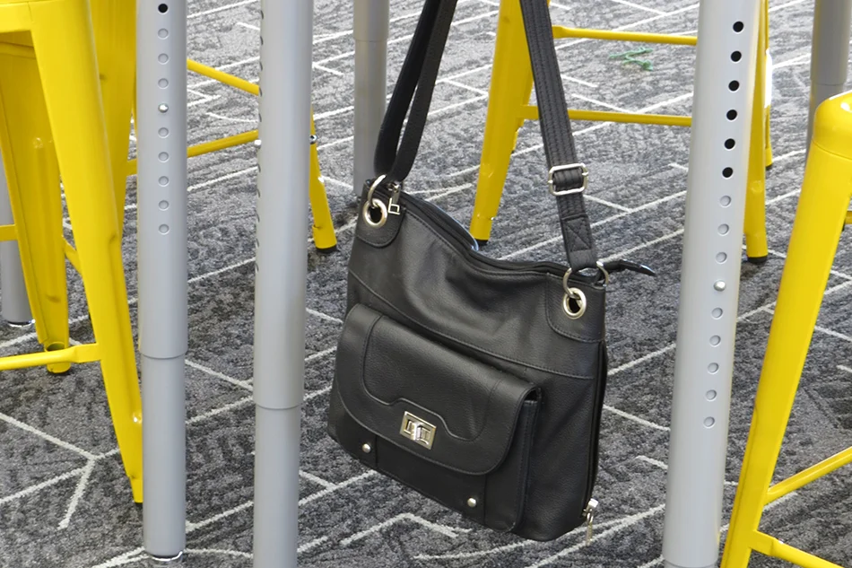 A purse handing on a hook attached to a student seating table