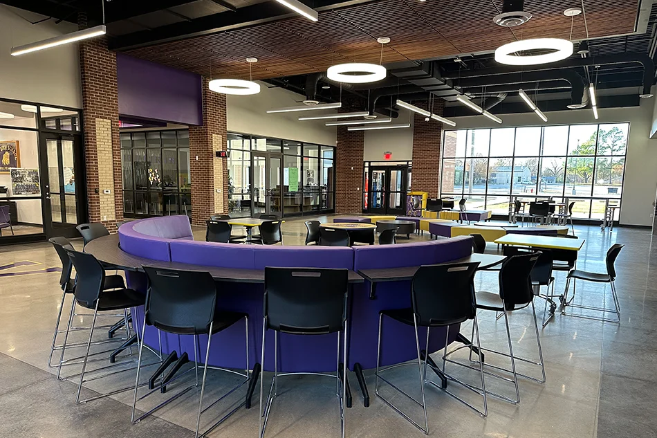 A purple round couch with a table attached on the back and stools surrounding it.